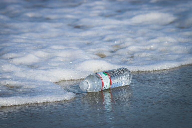 A plastic water bottle sits on a beach as a wave slowly creeps in