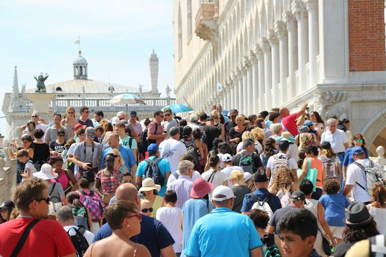 the scene is filled with crowds on people, we can assume they are standing in a town square as there are buildings with columns surrounding them