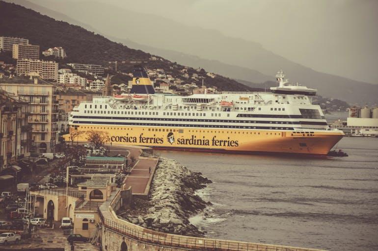 A large cruise ship sits docked at a city's marina. In the background are faint mountains on a cloudy day.