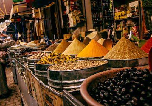 Spices are shown in containers at a market in Morocco, their colorful mounds forming conical pyramid shapes.