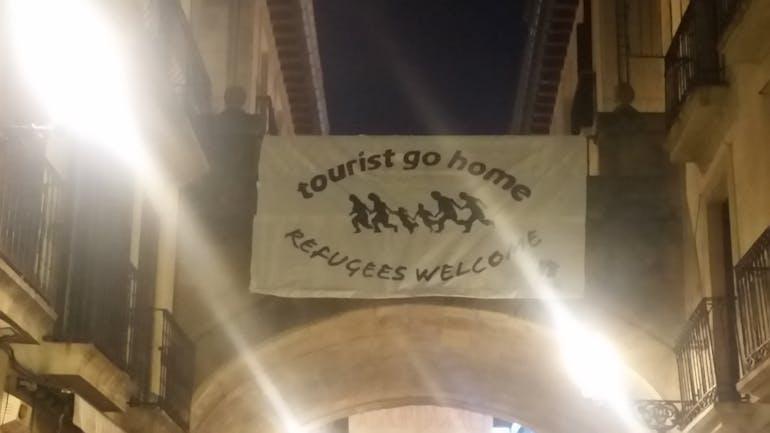 A banner hangs in Spain saying "tourist go home, refugees welcome". 