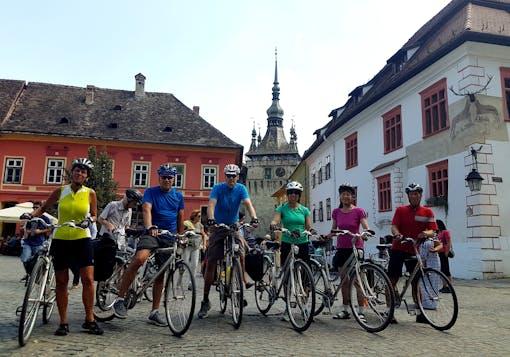 A group of bikers stand in a town square straddling their bikes in a rural town in Romania on a guided cycling tour.