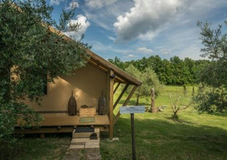 A small wooden house sits on a green field under a partly cloudy sky, this is the Sant’Egle Eco BIO Resort in Sorano Italy.