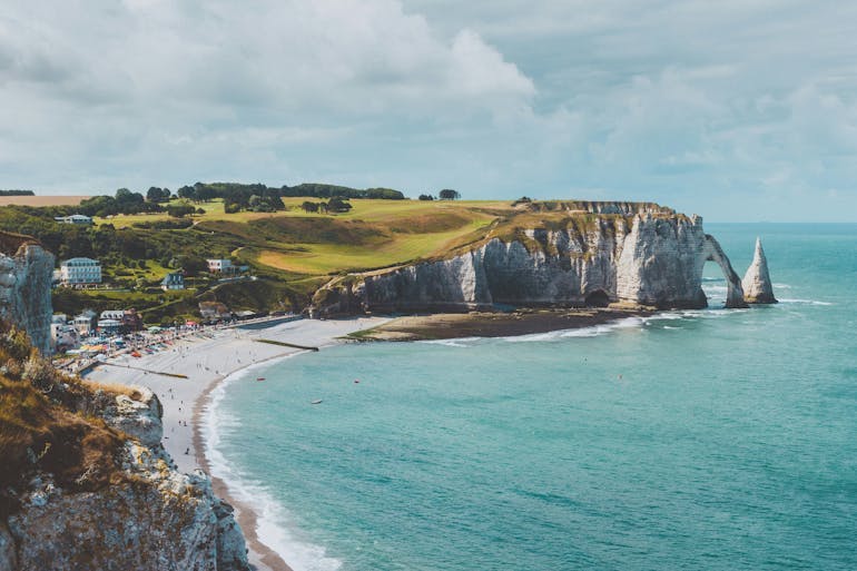The Normandy coast and white cliffs of Etretat. In the distance you can see the famous cliffs and rock formations with a rocky beach at the foot of the cliffs. 
