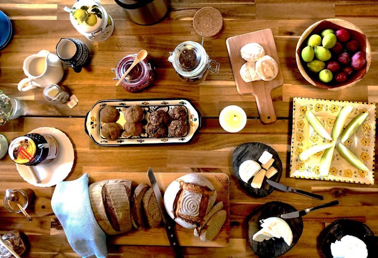 A healthy brunch display of fruit, breads, fruit, and more is laid out artfully across a table.