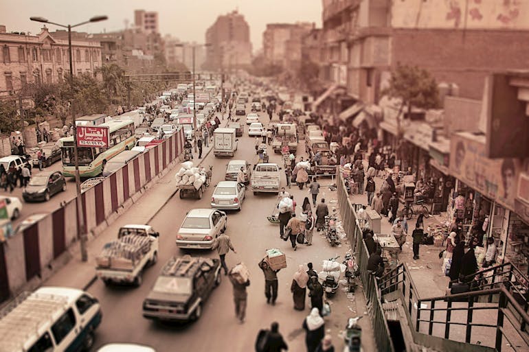 A sepia-toned photo shows an aerial view of a busy street in a hazy city crowded with people and cars.