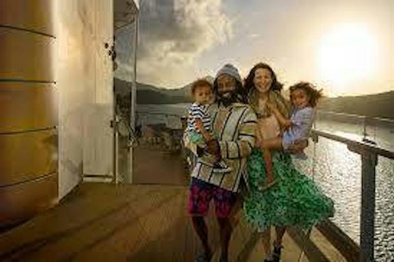A diverse family with an Indian dad, a Caucasian mom, and two mixed kids, one boy and one girl, stand on the deck of a cruise at sunset.