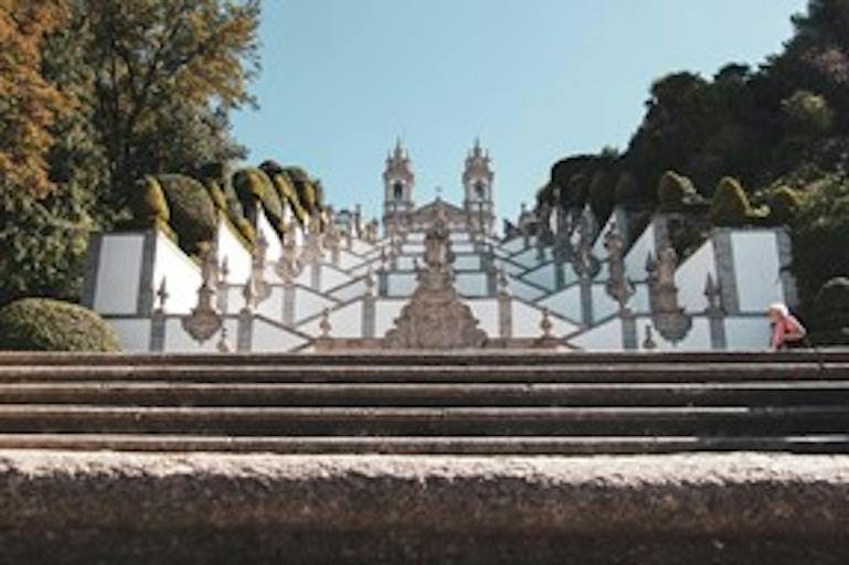 The Sanctuary of Bom Jesus do Monte in Portugal is shown from the ground, looking up a steep expanse of stairs leading to the temple on the top.